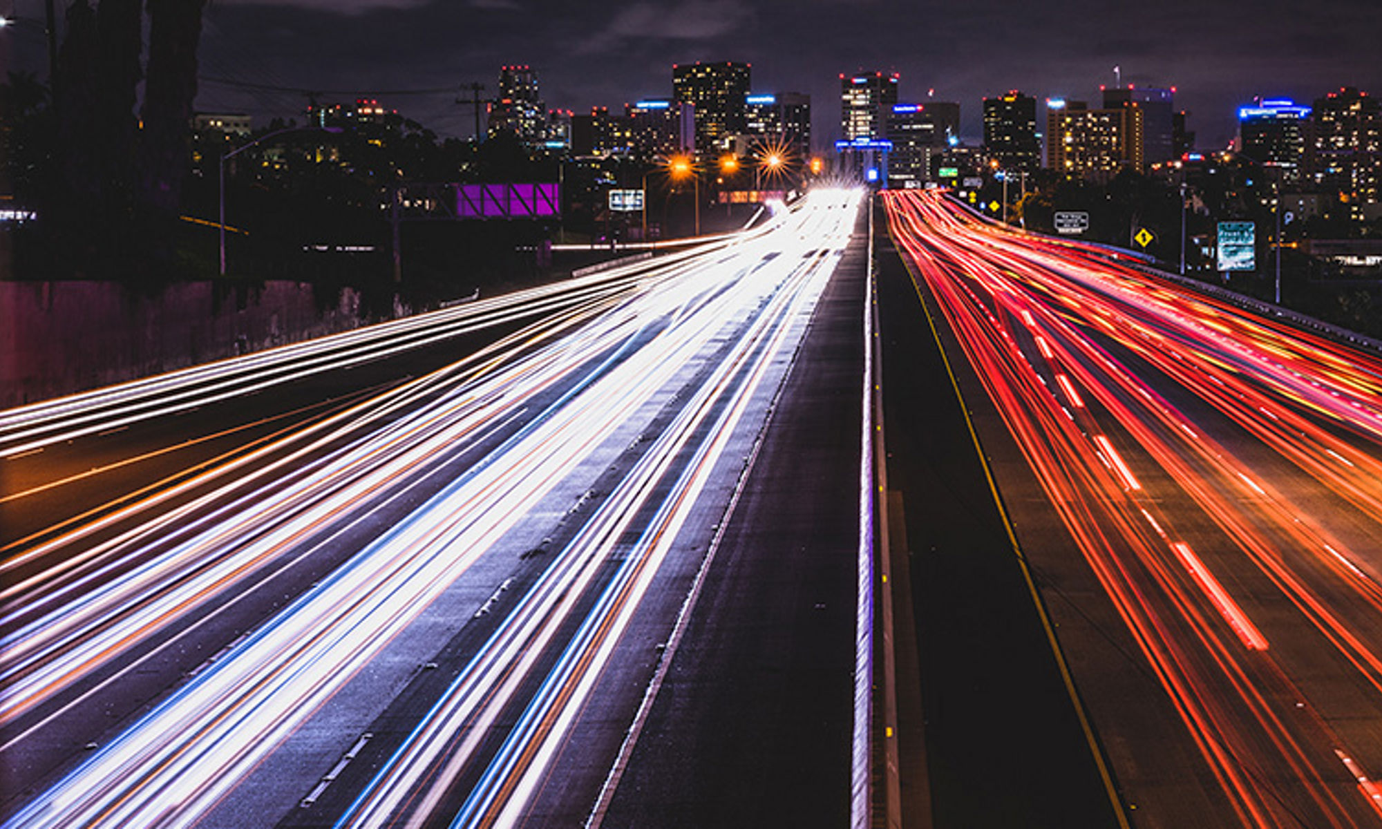 汽车在夜晚的高速公路上飞驰，前灯和尾灯射出光线，背景为一座城市