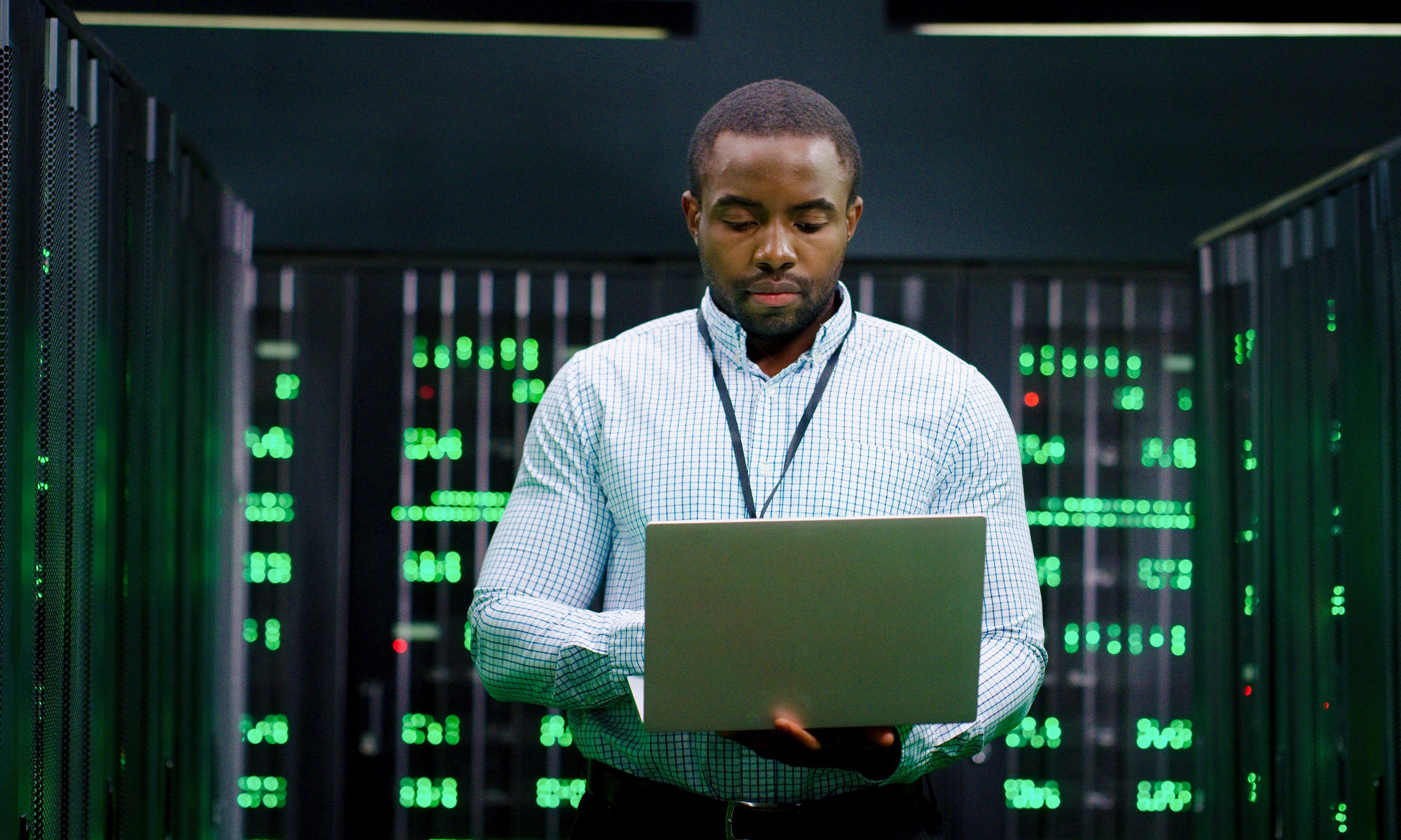 大型数据中心的男性系统管理员在服务器机房中工作，他的手在笔记本电脑上打字。编程数字化操作。在数据库中心在线工作的男工程师。电信。