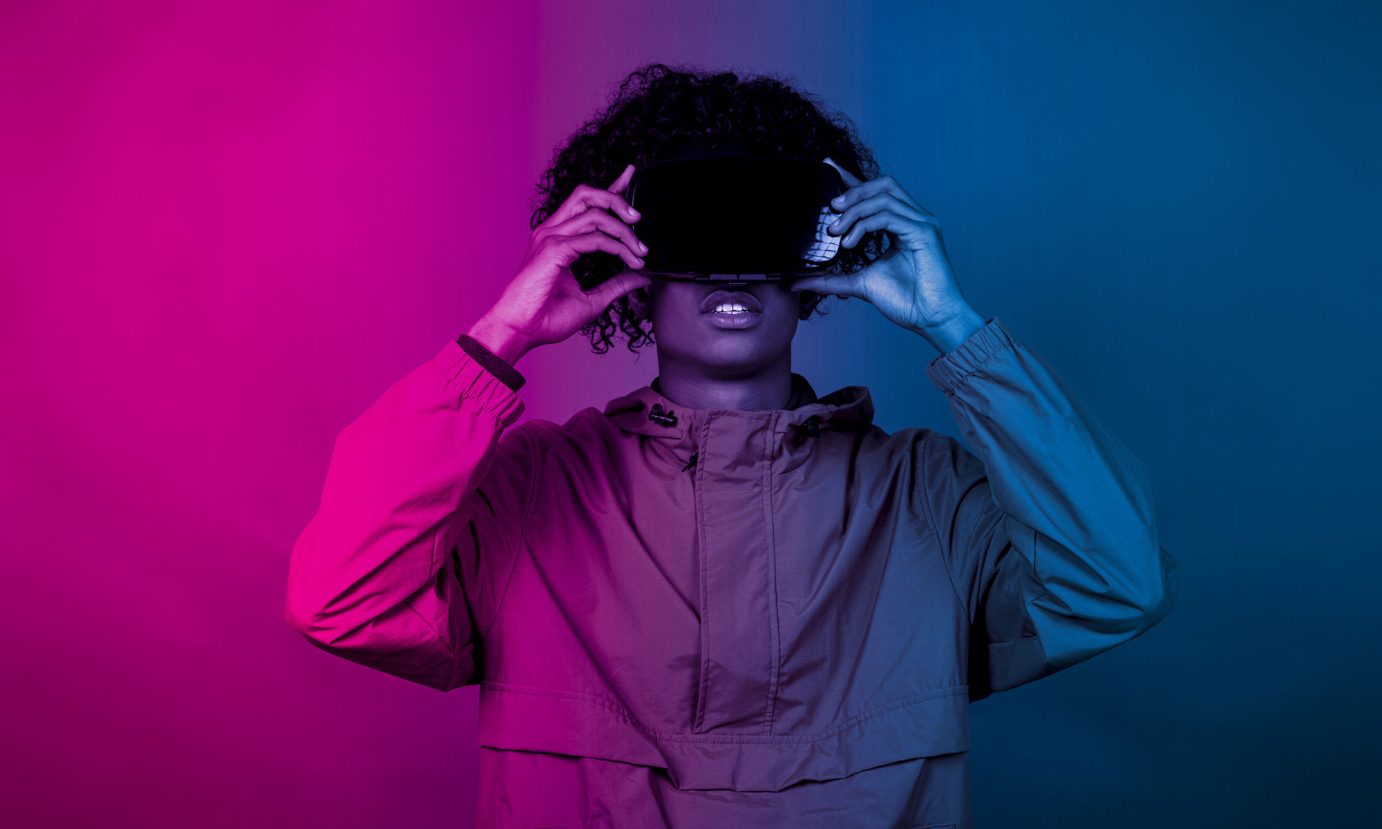 戴着 VR 眼镜的年轻非裔男士站在蓝色和紫色的灯光下
