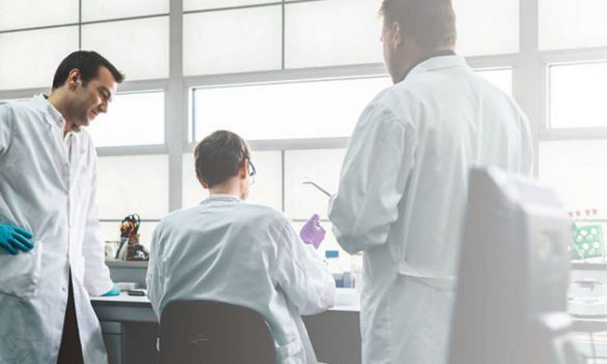Three co-workers in lab coats discussing something